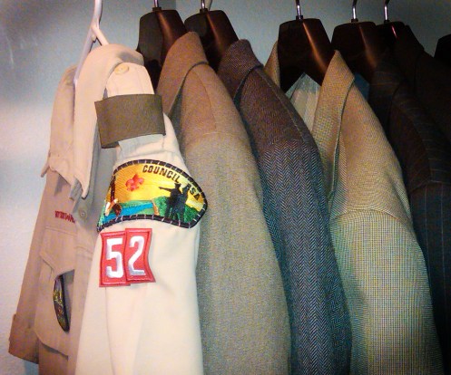 A Boy Scouts Leader shirt hangs in a closet alongside business attire